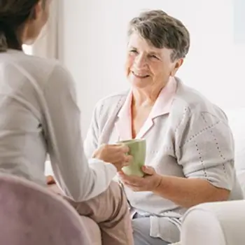 Bild einer Seniorin, der von einer Frau eine Tasse überreicht wird